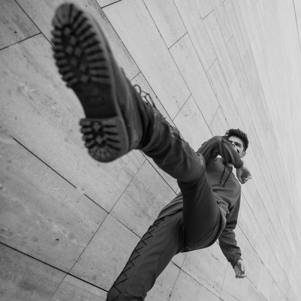 Dynamic man in urban cargo outfit performing high kick on city pavement