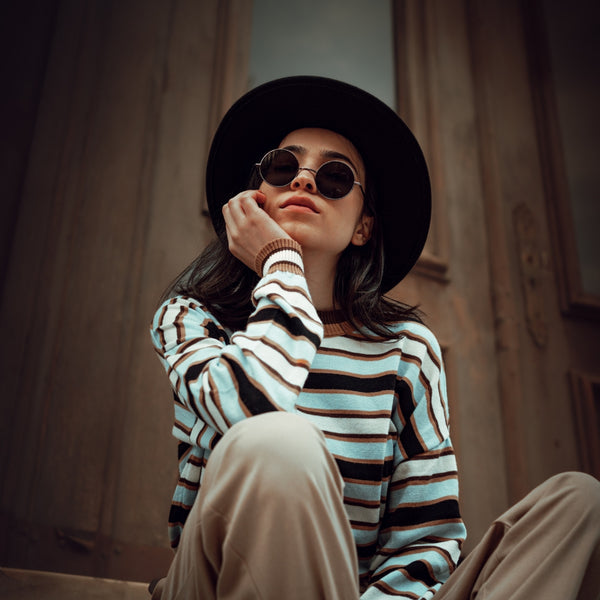 Stylish woman in striped long sleeve top and wide brim black hat sitting